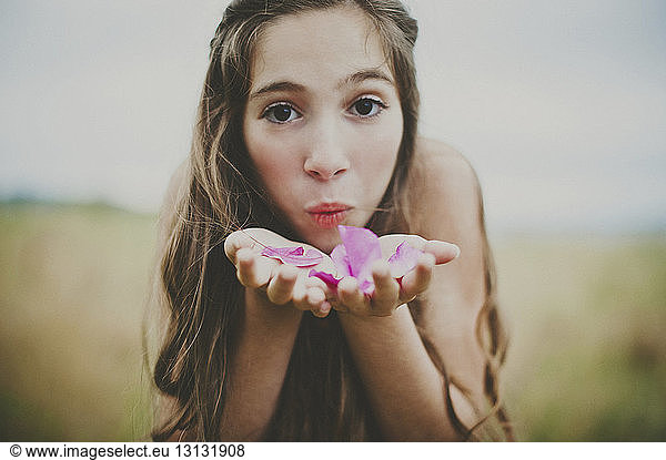 Portrait of happy girl blowing pink flower petals on field