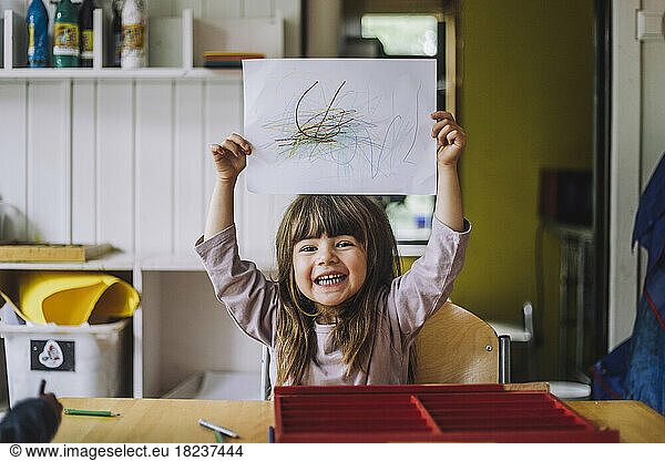 Portrait of happy girl showing color pencil scribble on paper at kindergarten