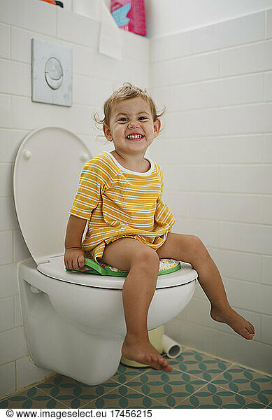 Portrait of happy girl sitting on toilet at home Portrait of happy girl ...