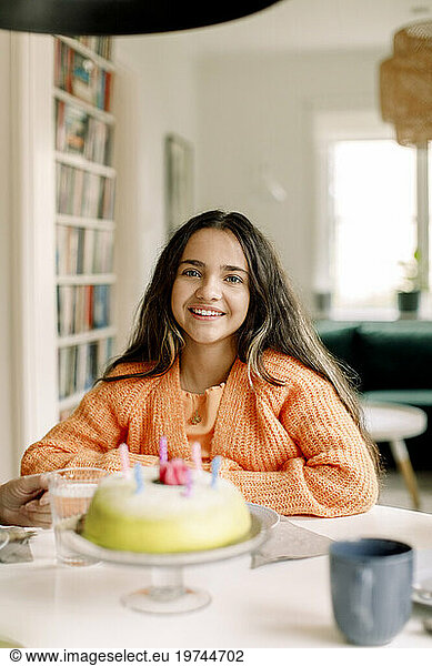 Portrait of happy girl sitting with birthday cake at dining table