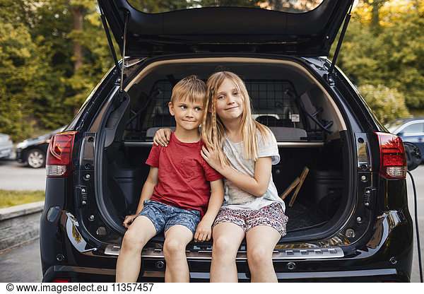 Portrait of happy girl sitting with brother in car trunk