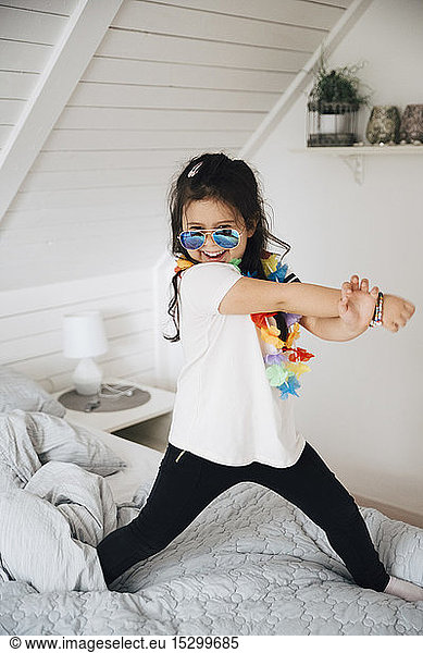 Portrait of happy girl wearing sunglasses dancing on bed at home