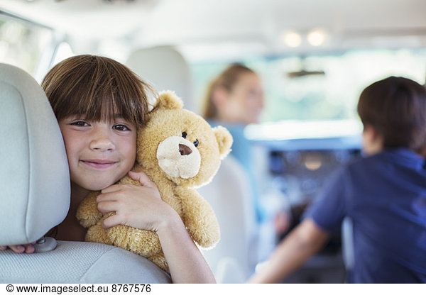 Portrait of happy girl with teddy bear in back seat of car