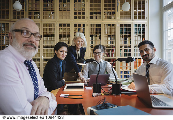 Portrait of happy lawyers at table against bookshelf