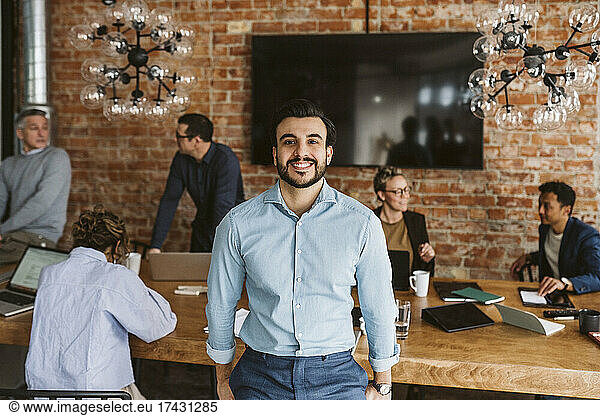 Portrait of happy male professional standing while colleagues discussing in background