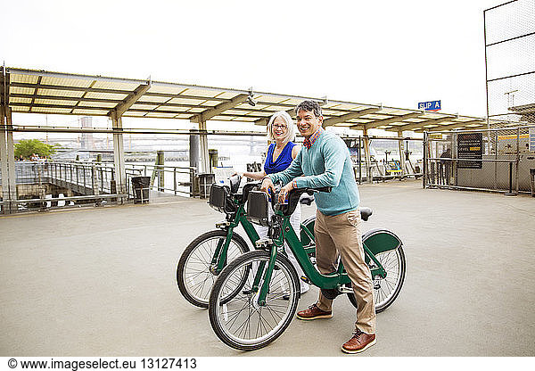 Portrait of happy mature couple standing with bicycles on footpath