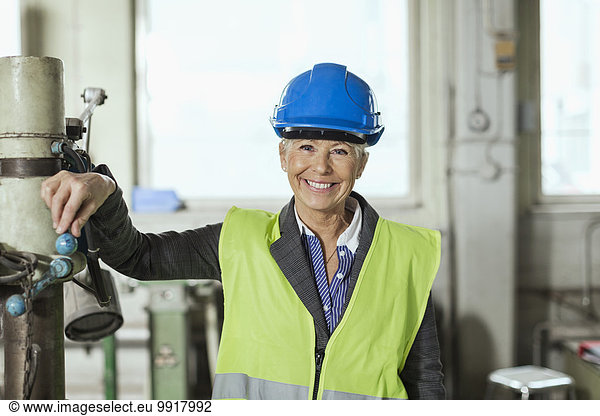 Portrait of happy mature female worker wearing hardhat in factory