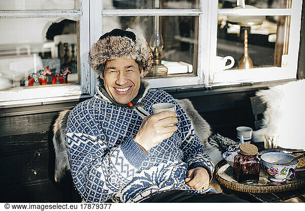 Portrait of happy mature man having coffee while sitting at porch during winter