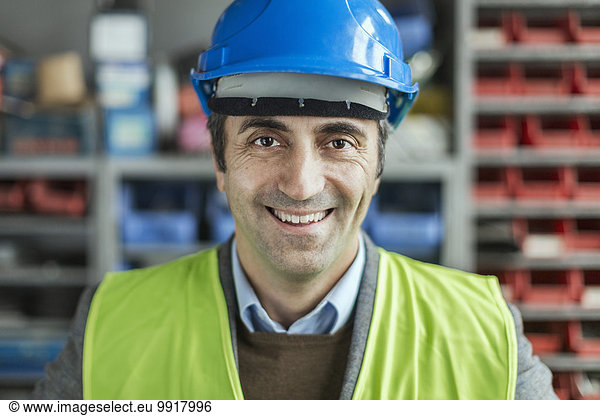 Portrait of happy mature manual worker wearing hardhat in factory