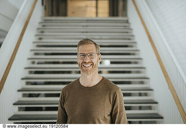Portrait of happy mature professor standing against steps in university