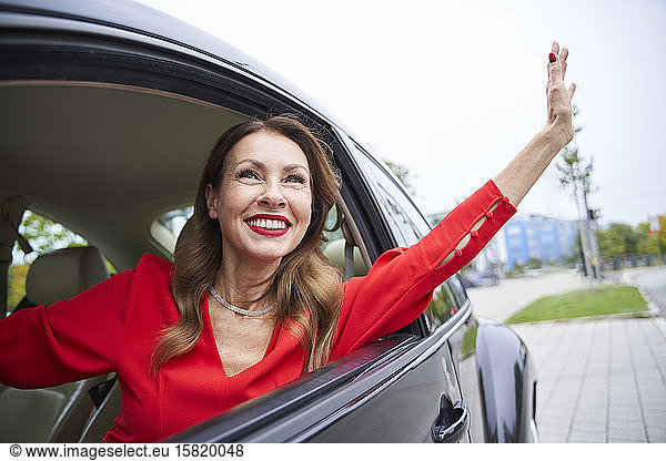 Portrait of happy mature woman looking out of car window waving