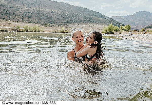 Portrait of happy mom and daughter playing in a lake on a sunny day
