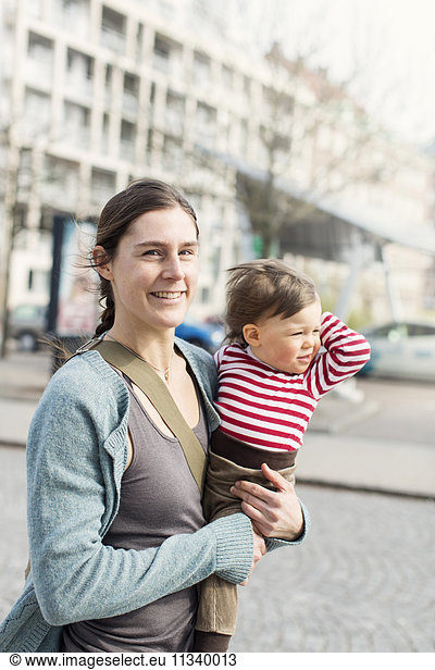 Portrait of happy mother carrying baby girl in city