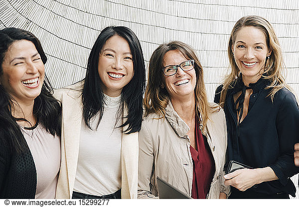 Portrait of happy multi-ethnic female business professionals standing against wall