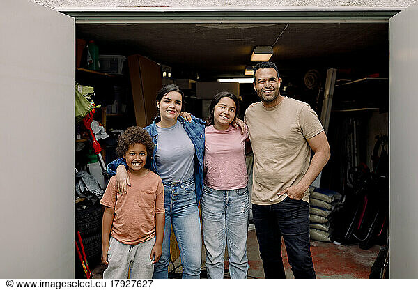 Portrait of happy multiracial family standing with arms around outside storage room