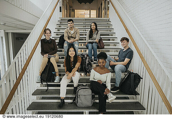 Portrait of happy multiracial male and female students sitting on staircase in university