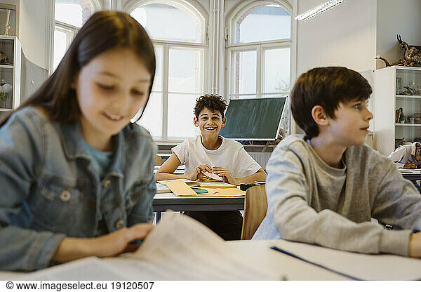 Portrait of happy schoolboy sitting at desk with friends in classroom