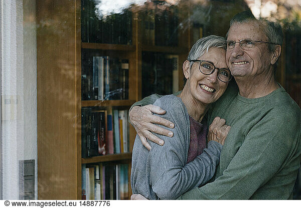Portrait of happy senior couple hugging behind windowpane