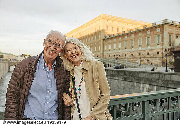 Portrait of happy senior man and woman leaning on railing in city