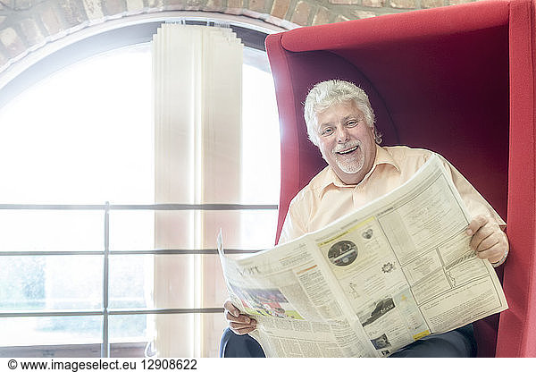 Portrait of happy senior man with newspaper in a city library