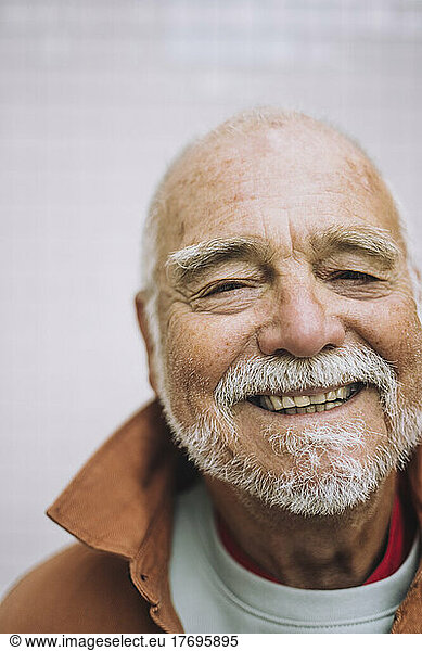 Portrait of happy senior man with white beard against wall