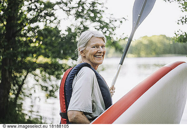 Portrait of happy senior woman holding paddleboard and oar