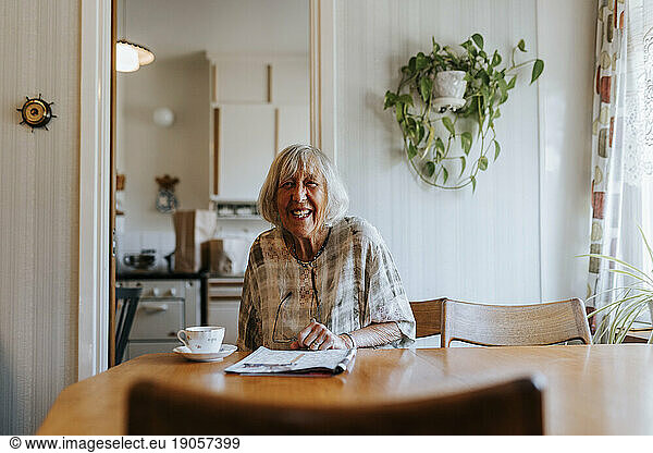 Portrait of happy senior woman sitting at dining table in home