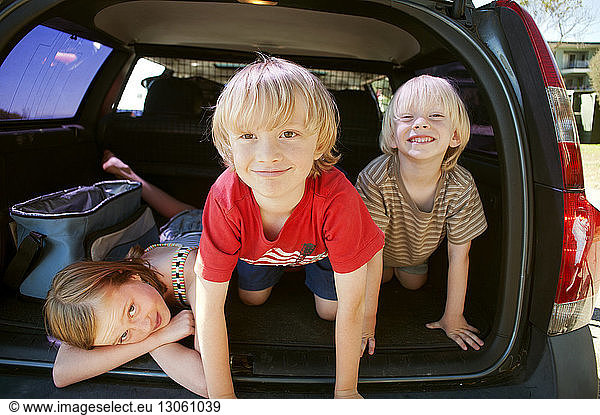 Portrait of happy siblings in car trunk