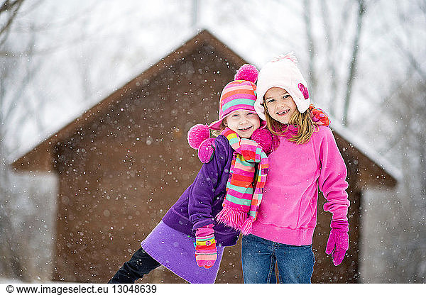 Portrait of happy sisters standing outdoors during snowfall