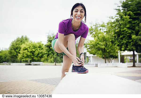 Portrait of happy sporty woman wearing shoes on footpath