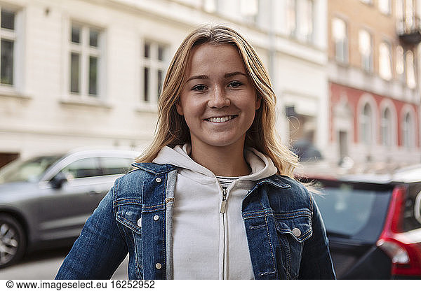 Portrait of happy teenage girl standing in city during weekend
