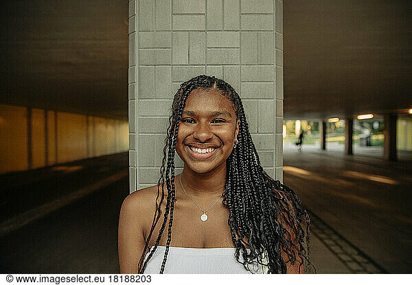 Portrait of happy teenage girl with braided hair standing against column