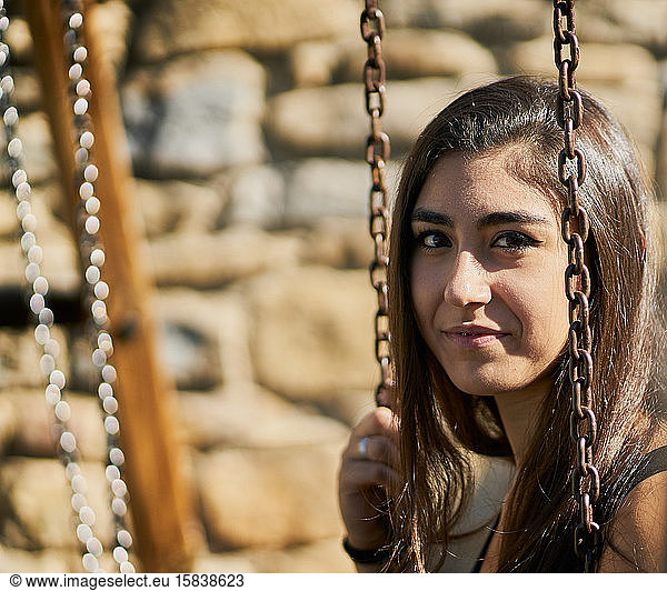 portrait of happy teenage girl with brown hair is sitting on a swing