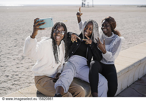 Portrait of happy teenage girlfriends taking a selfie at the beach