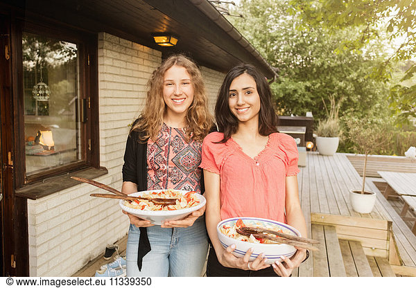 Portrait of happy teenage girls holding salad bowls outside house at yard