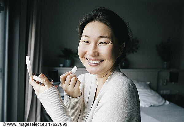 Portrait of happy woman applying make-up in bedroom at home