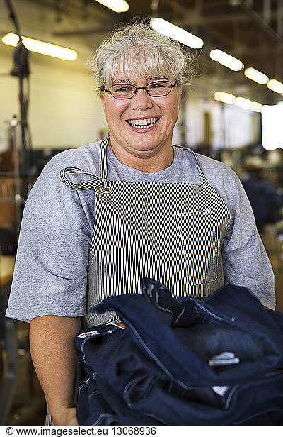 Portrait of happy woman carrying denim clothing in factory