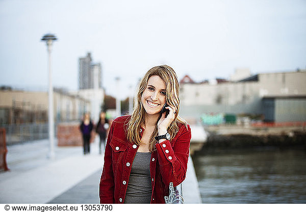 Portrait of happy woman communicating on phone while standing on promenade
