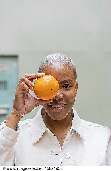 Portrait of happy woman covering her eye with an orange outdoors