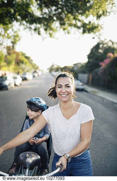 Portrait of happy woman holding bicycle with son sitting on back seat