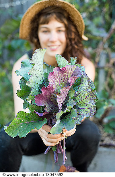 Portrait of happy woman holding leaf vegetables while sitting in garden