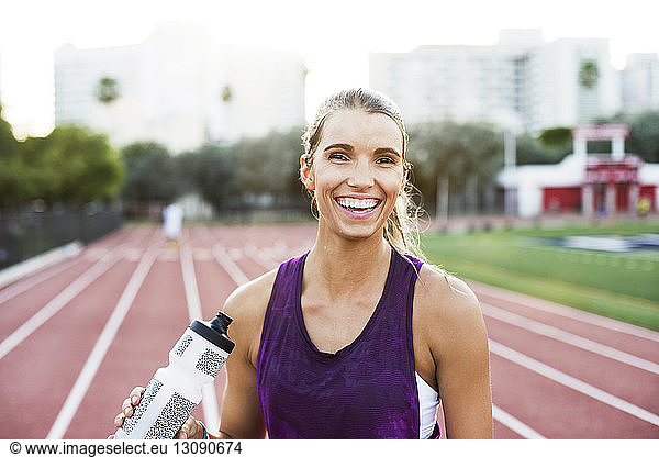 Portrait of happy woman holding water bottle on race tracks
