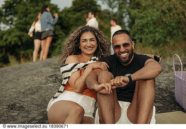 Portrait of happy woman sitting on rock with man wearing sunglasses during picnic