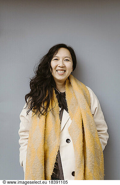 Portrait of happy woman wearing warm clothing while standing against gray background
