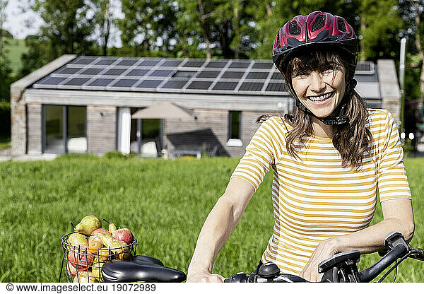 Portrait of happy woman with bicycle and organic fruit on a meadow in front of a house