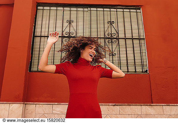 Portrait of happy woman with red dress  dancing in front of a red wall