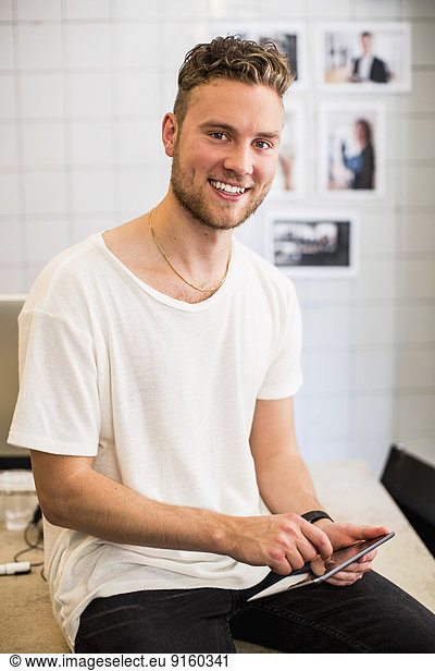 Portrait of happy young businessman using digital tablet in new office