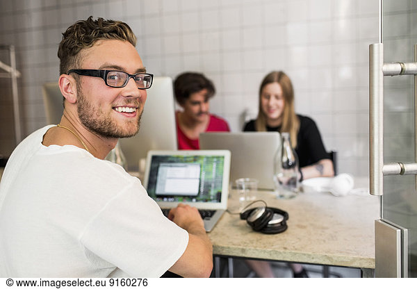 Portrait of happy young businessman with colleagues in background at creative office