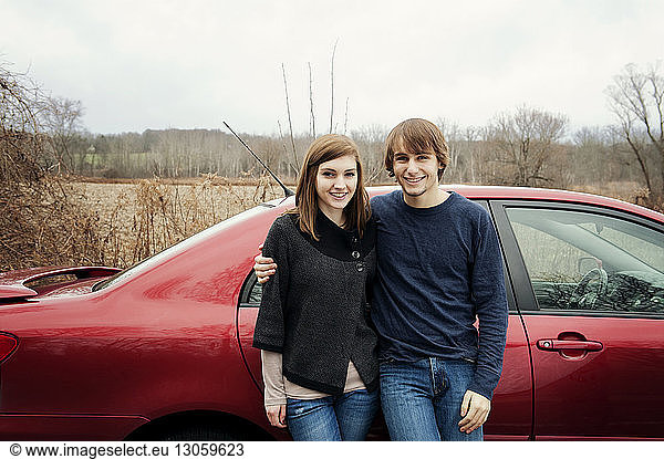 Portrait of happy young couple standing against car