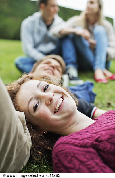 Portrait of happy young girl with head on boy's stomach and couple sitting in background at park